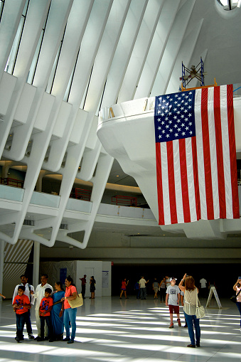 New York City, USA - July 02, 2016: People posing for photos nearby large American flag under The Oculus,  World Trade Center Transportation Hub at Ground Zero, World Trade Center site, Lower Manhattan.