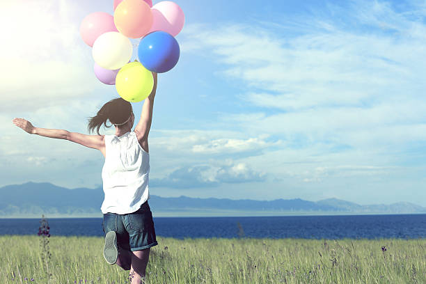 istock cheering young woman running on grassland with colored balloons 577655746