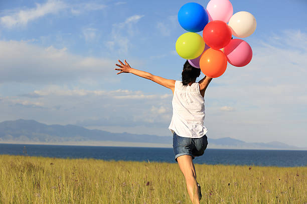 istock cheering young woman running on grassland with colored balloons 577659458