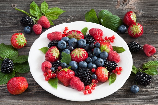 White plate with fresh berries on wood background