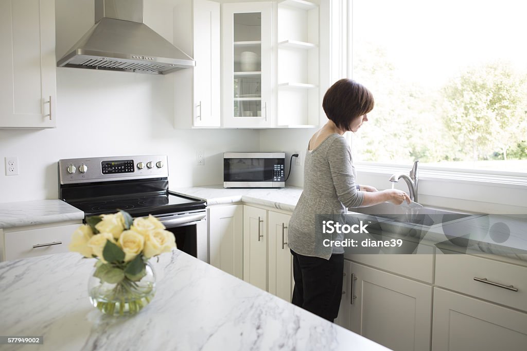 Woman Working in a Modern Kitchen A woman washes a dish at a sink in a modern kitchen. Cleaning Stock Photo