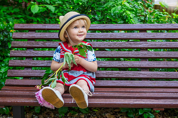 beautiful toddler girl sitting on a bench holding a flower