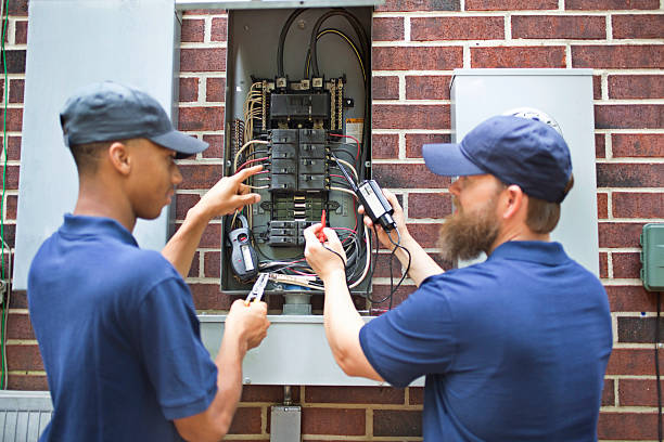 Repairmen, electricians working on home breaker box. Two men electricians working on a residential breaker box.  They use tools to assess the repair and wear matching blue uniforms.  The multi-ethnic group is discussing next steps in the job repair.  Electric meter to side. fuse box stock pictures, royalty-free photos & images