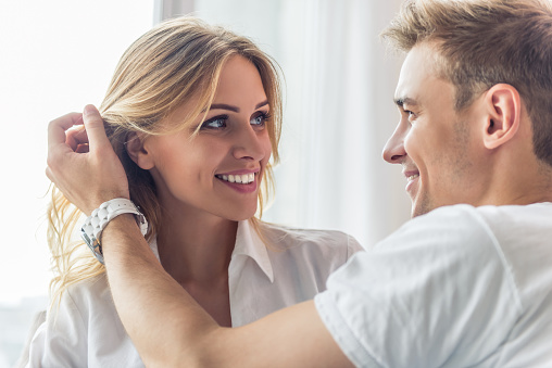 Portrait of beautiful young couple looking at each other and smiling while sitting at home. Man is smoothing his girlfriend's hair