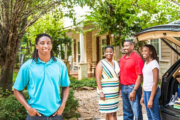 African descent boy heads off to college or moves away from home.  The 18-year-olds' parents and sister are all helping him pack up his car as he gets ready for the big move.  He is excited to start his college adventures. Family events.  Back to school.