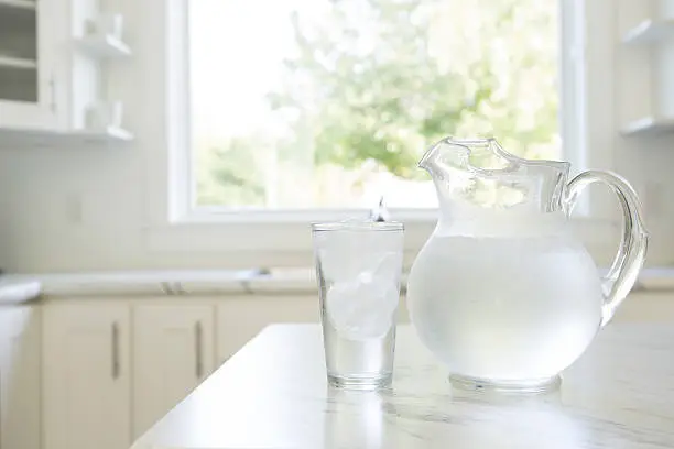 A water pitcher and glass on a kitchen countertop