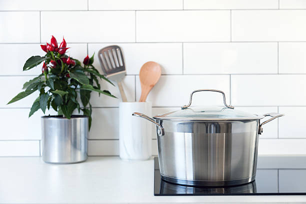 Pot on kitchen induction cooktop Large pot sits on an induction hob, with cooking utensils and Thai Chili plant in the background against subway tile splashback electromagnetic induction stock pictures, royalty-free photos & images