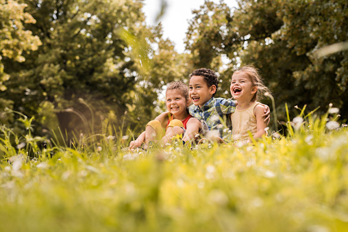 Three small children sitting embraced in grass and enjoying in nature.