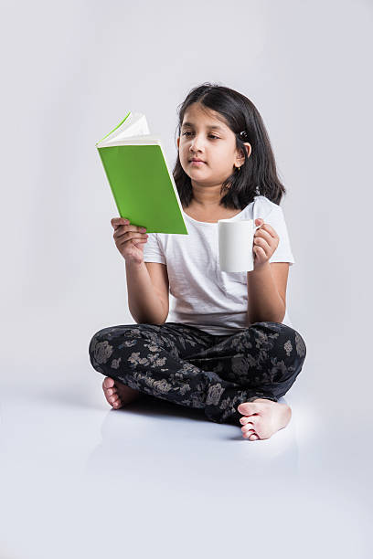 istock indian small girl child reading book on ground 577973472