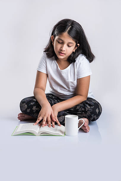 istock indian small girl child reading book on ground 577973604