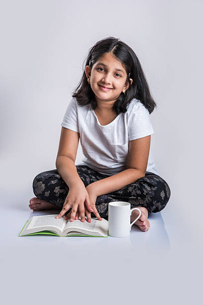 istock indian small girl child reading book on ground 577973742