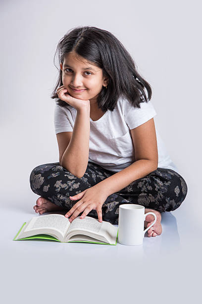 indian small girl child reading book on ground