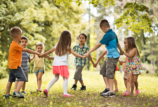 Large group of little children holding hands and playing ring-around-the-rosy in nature.