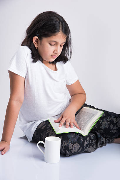 istock indian small girl child reading book on ground 577974472