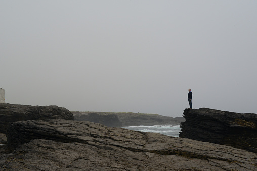 Single hiker on cliff edge on an overcast day in summer, Hook Head, Wexford, Ireland. 