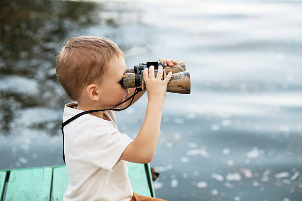 маленький мальчик, смотрящ через бинокль на берегу реки - little boys discovery binoculars child стоковые фото и изображения