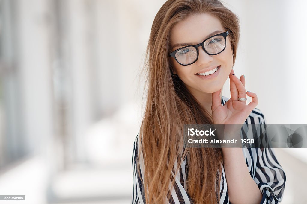 Portrait of a happy woman in spring city Portrait of happy woman in glasses in spring city,blonde long straight hair,blue eyes,beautiful white teeth and nice smile,light makeup,wearing a thin striped blouse with white and black stripes,spends time in the city enjoying the Sunny day Adult Stock Photo