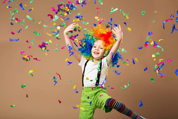 Little boy in clown wig jumping and having fun Little boy in clown wig jumping and having fun celebrating birthday. Portrait of a child throws up a multi-colored tinsel and confetti. Birthday boy. Positive emotions. carnival children stock pictures, royalty-free photos & images