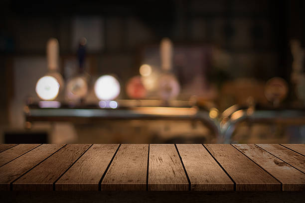 wooden table with a view of blurred beverages bar backdrop wooden table with a view of blurred beverages bar backdrop pub stock pictures, royalty-free photos & images