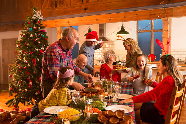 Christmas Dinner A large family are all helping serve Christmas dinner. big family table stock pictures, royalty-free photos & images