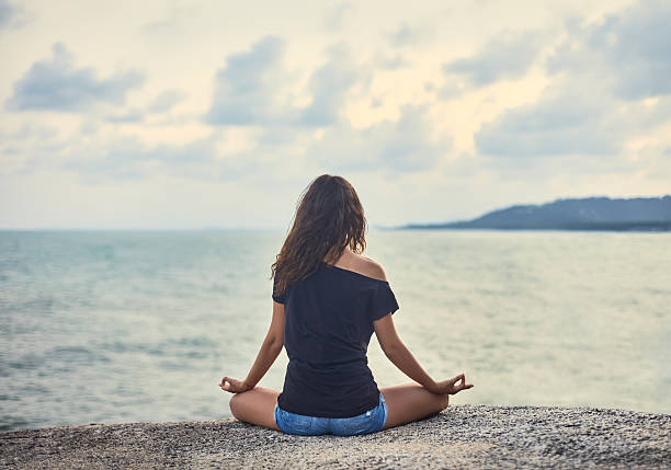 istock Woman meditating on rocky cliff with sea view 578098356