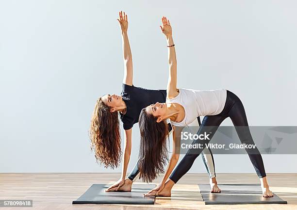 Two Young Women Doing Yoga Asana Extended Triangle Pose Stock Photo - Download Image Now