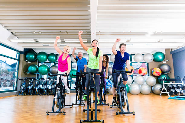 Group of men and women exercising on fitness bikes Group of men and women exercising on fitness bikes in gym, diversity people, old, young, black and white spin bike stock pictures, royalty-free photos & images