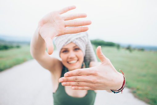 Cheerful young woman having fun on the road, making finger frame. With towel on head. Looking at camera. Landscape and sky on background. Focus on foreground.