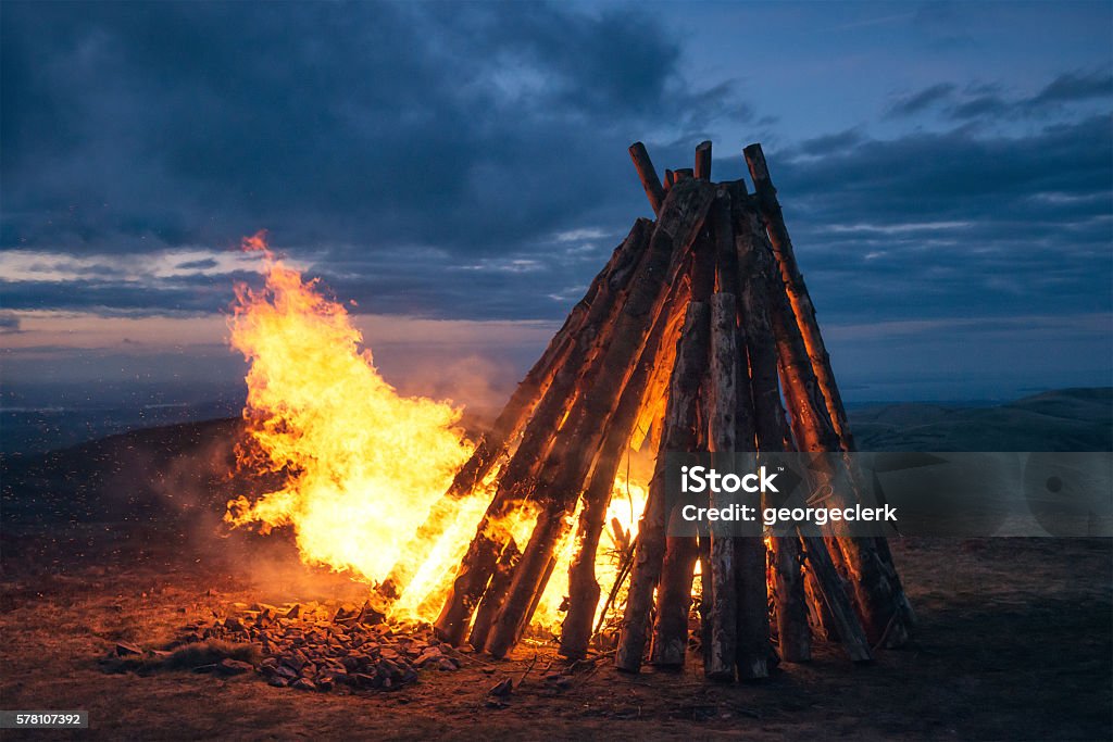 Large fire beacon burning on hilltop Flames and sparks from a large fire on a rural hilltop, lighting up the sky at twilight. Bonfire Stock Photo