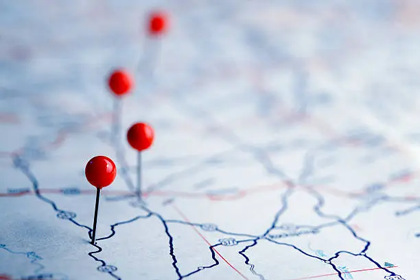 A row of four push pins on a road map.  The road map is very generic with no town names or landmarks legible.  The image is photographed using a very shallow depth of field.