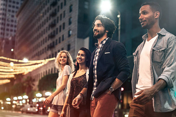 City Life Friends at Night A group of multi-ethnic young adults explore and walk around downtown Los Angeles, California on a summer evening, checking out the city night life.  They walk casually down a city street lined with cars and tall buildings, talking and enjoying the night.  Horizontal image. nightlife stock pictures, royalty-free photos & images