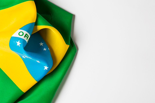 A photograph of the Brazilian national flag laying on a plain white background. There is space for text.