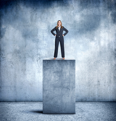 A businesswoman proudly stands with her hands on her hips as she stands on top of a large concrete pedestal.