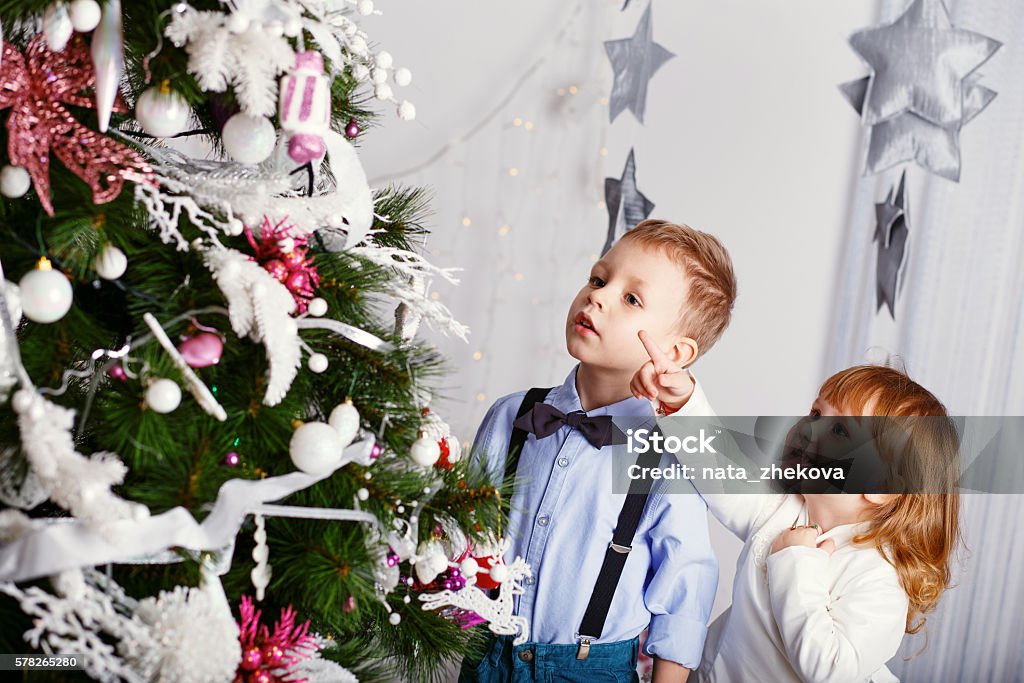 Two little kids decorating Christmas tree with toys, flowers and Two little kids decorating Christmas tree with toys, flowers and balls. New year preparation. Happy children and family. Anticipation Stock Photo