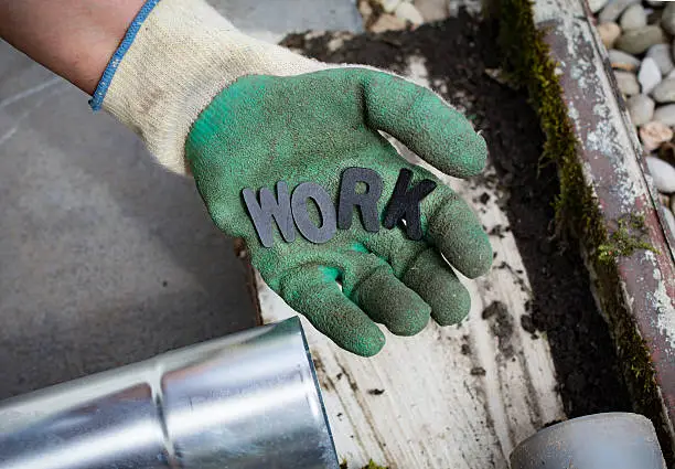 Holding up a Work   glove with the word work in wooden letters and new and old drainpipes on the floor