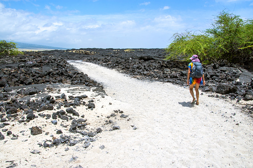 Woman hiking a coral white sand trail through black lava rock. Big Island, Hawaii.