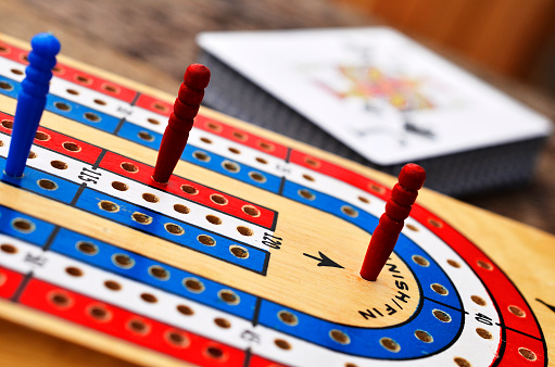 A close up image of a red, white, and blue cribbage board with the Jack of Spades card in the background.