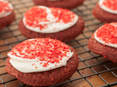 Studio photo of stack of red velvet shortbread cookies on metal cooling rack. Selective focus on red sprinkles on main cookie on right.