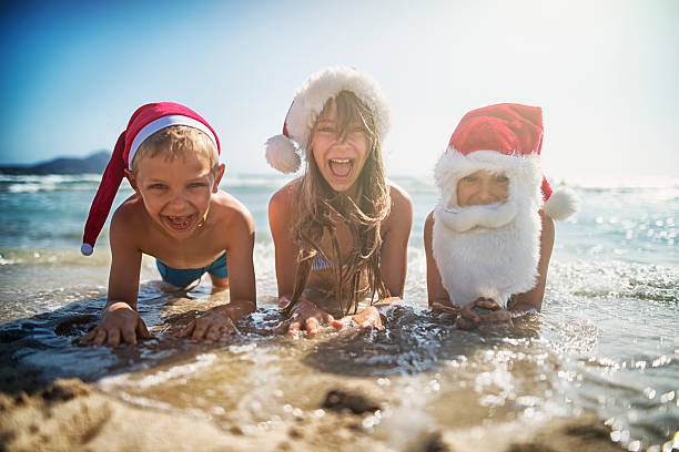 Christmas on the beach It's christmas on the beach. Kids wearing santa hats having fun on beach - laughing and screaming in water. girls laying on beach stock pictures, royalty-free photos & images