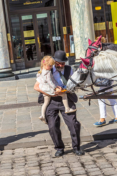 Vienna, Austria - April 27, 2015: coachman of traditional horse riding in vienna helps a young girl to feed the horses.  The number of horse riders is limited and they have a special licence.