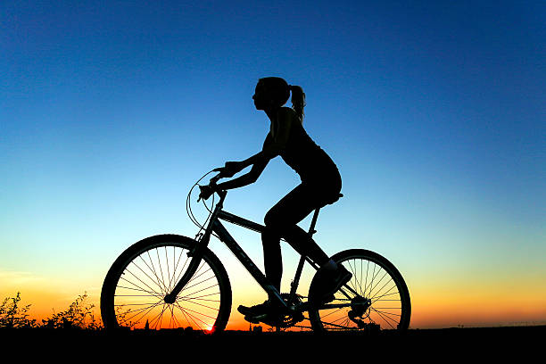 Silhouette of a female riding her bicycle. Unrecognizable young woman, slim with ponytail.
