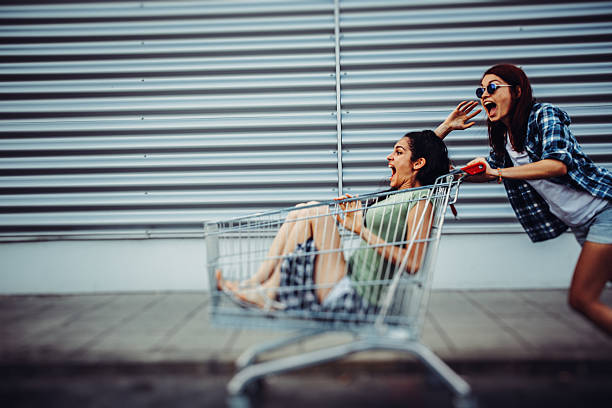 Two young girls having fun with a shopping cart on the street.