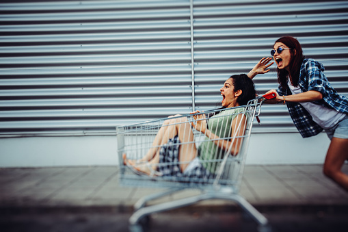 Two young girls having fun with a shopping cart on the street.