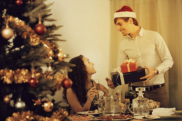 Couple giving presents at Christmas dinner Cheerful young man giving present to excited girlfriend during romantic Christmas dinner with champagne in home wonderingly stock pictures, royalty-free photos & images