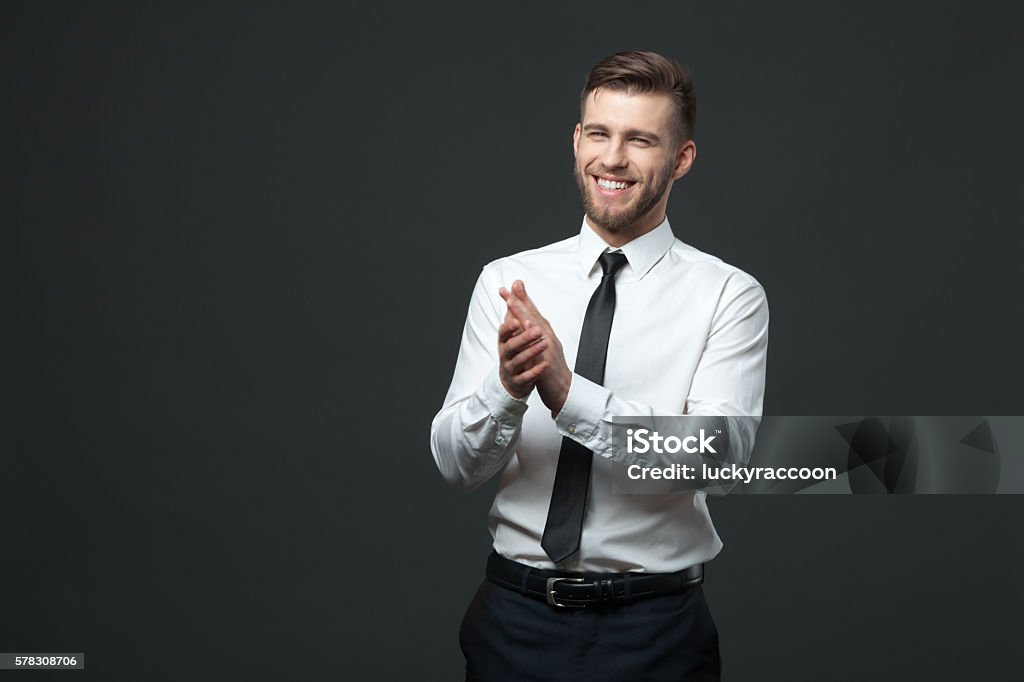 Studio portrait of young happy handsome businessman claping hands. Studio portrait of young happy handsome businessman claping hands isolated on dark background. Clapping Stock Photo