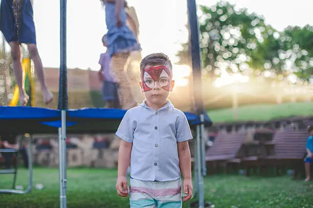 little boy with spiderman face paint by the trampoline , on a kids birthday