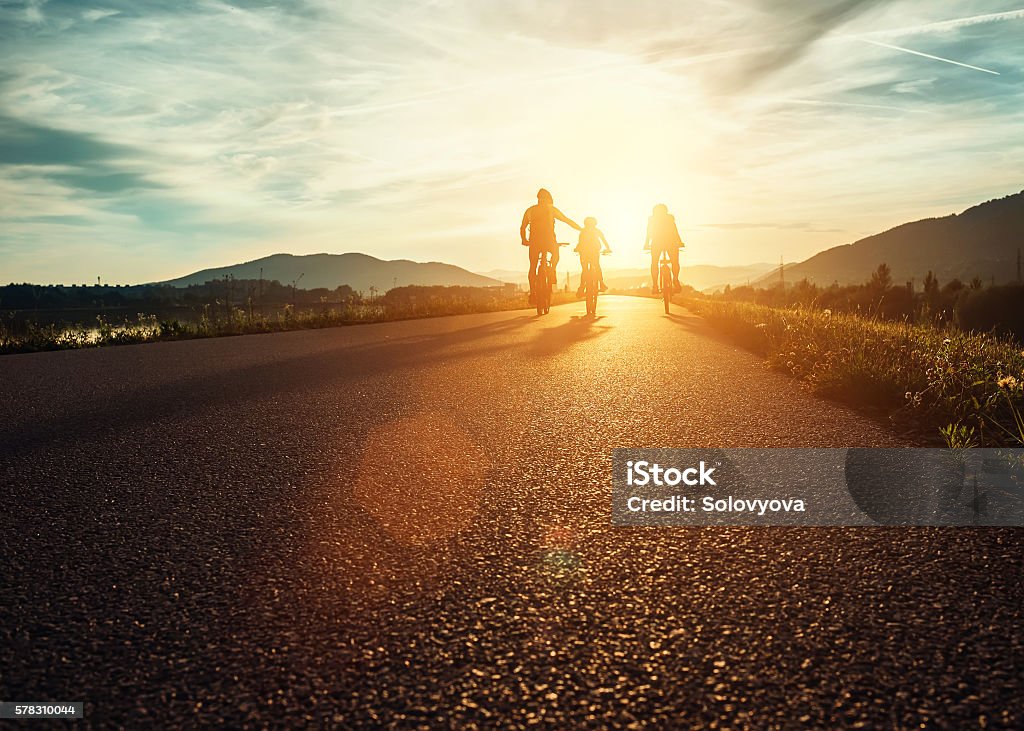 Famiglia Сyclists che viaggia sulla strada al tramonto - Foto stock royalty-free di Famiglia