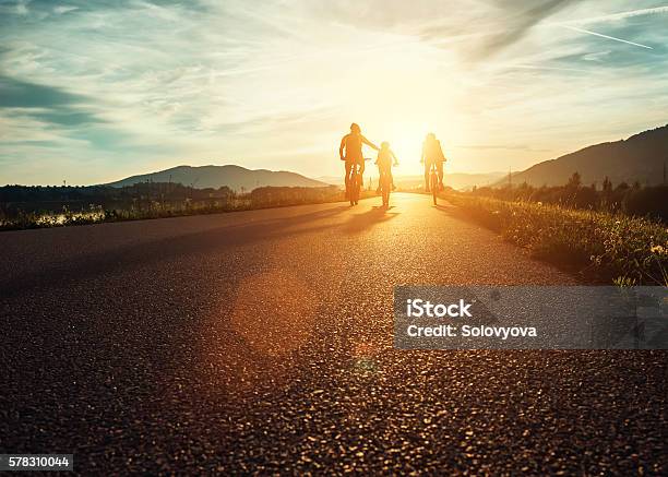 Сyclists Family Traveling On The Road At Sunset Stock Photo - Download Image Now - Family, Cycling, Sunset