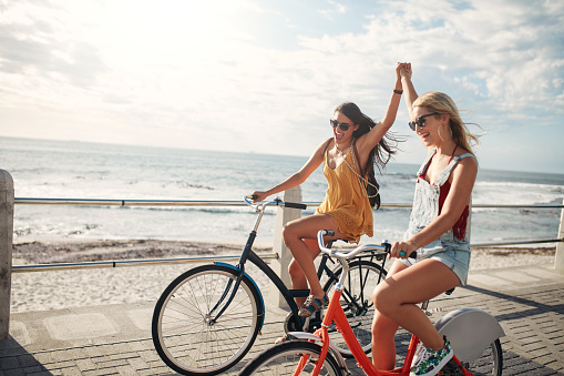 Female friends enjoying cycling on a summer day. Two young female friends riding their bicycles on the seaside promenade.