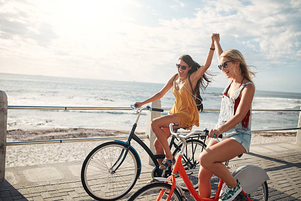 Female friends enjoying cycling on a summer day Female friends enjoying cycling on a summer day. Two young female friends riding their bicycles on the seaside promenade. cycling photos stock pictures, royalty-free photos & images